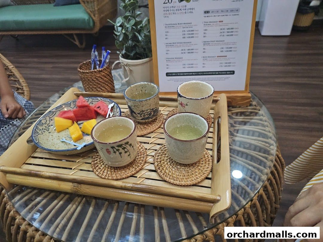 A tray with fruit and tea sits on a glass table, with a spa menu in the background.