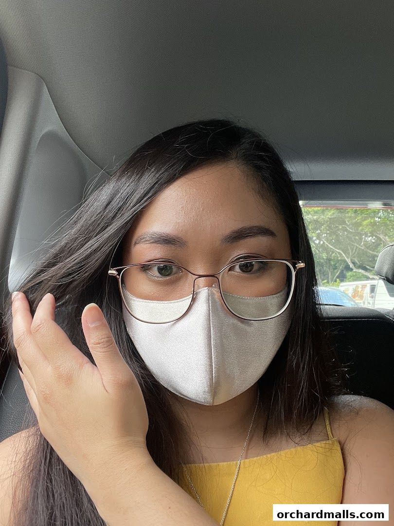 A woman wearing glasses and a face mask poses for a selfie in a car.