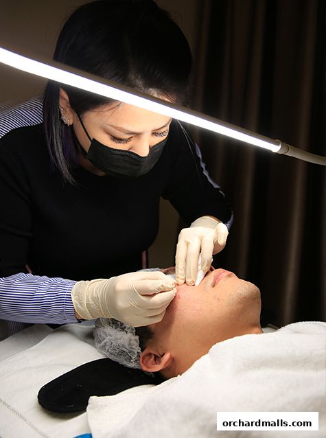 A beautician performs a facial treatment on a client under bright lighting.