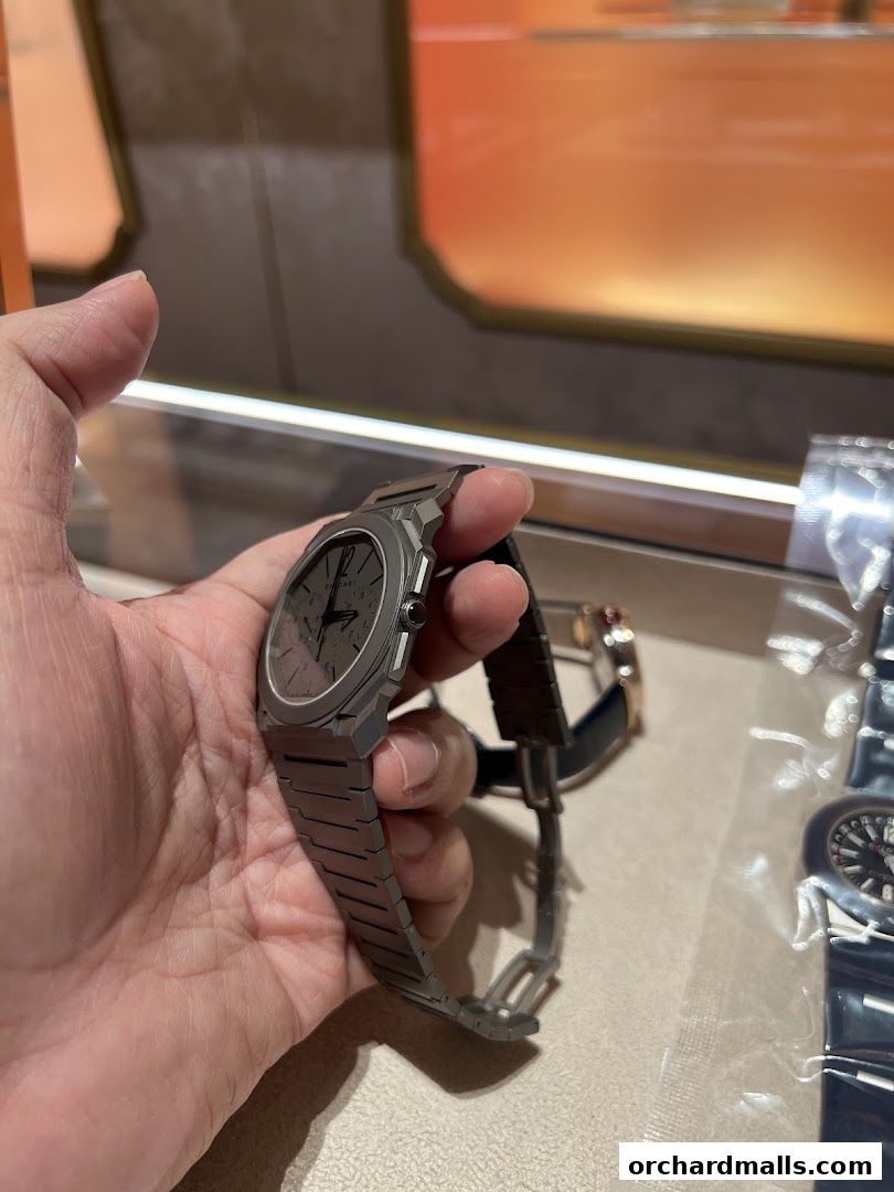 A hand holds a sleek, modern watch with a metal band in a retail display.