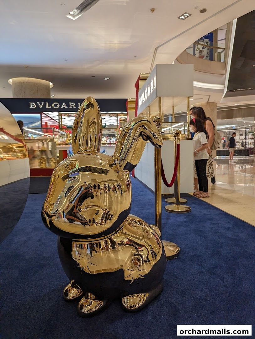 A golden rabbit sculpture is displayed in front of a Bulgari store with shoppers nearby.