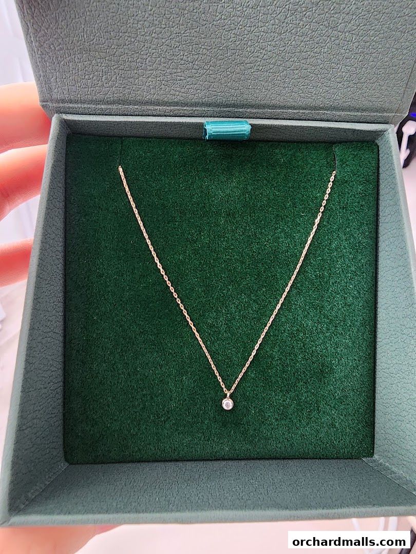 A delicate gold necklace with a single diamond pendant in a green jewelry box.