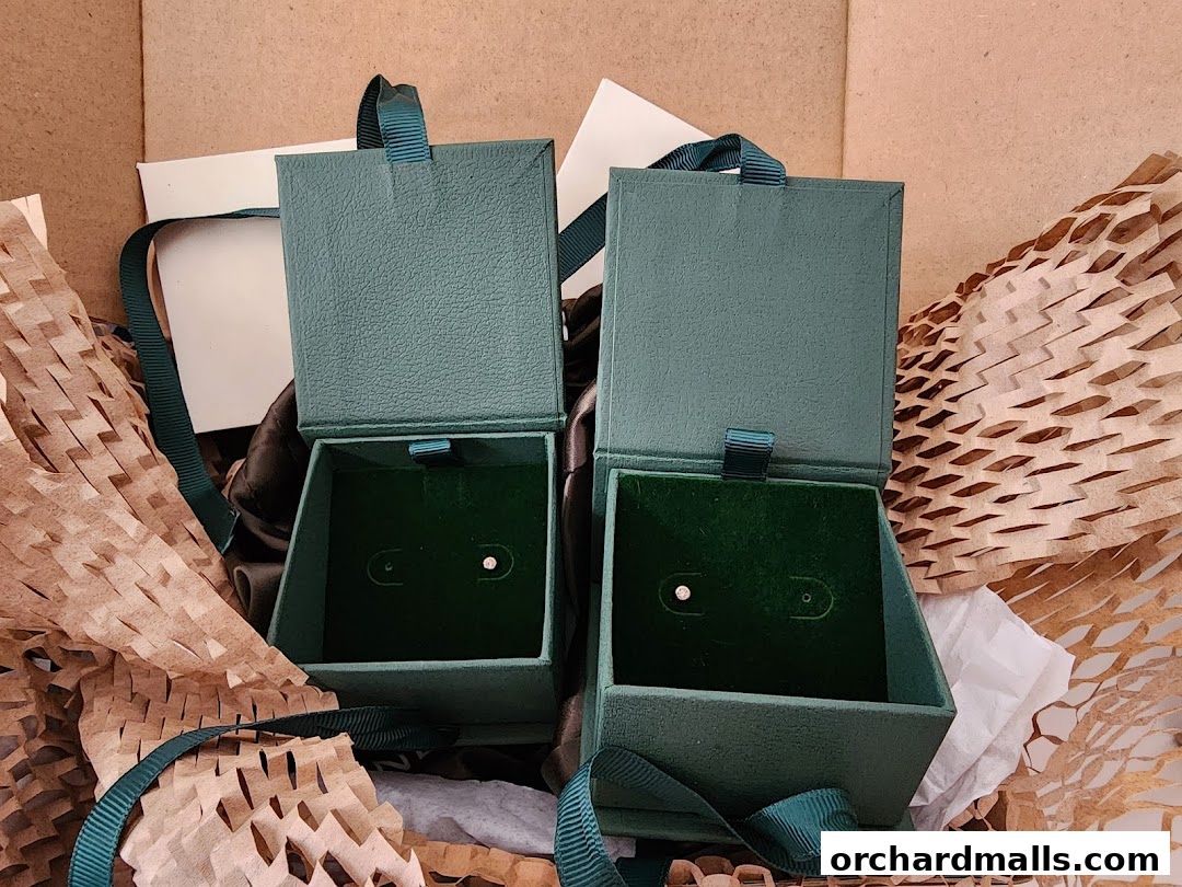 Two open jewelry boxes with small earrings inside, surrounded by packaging.