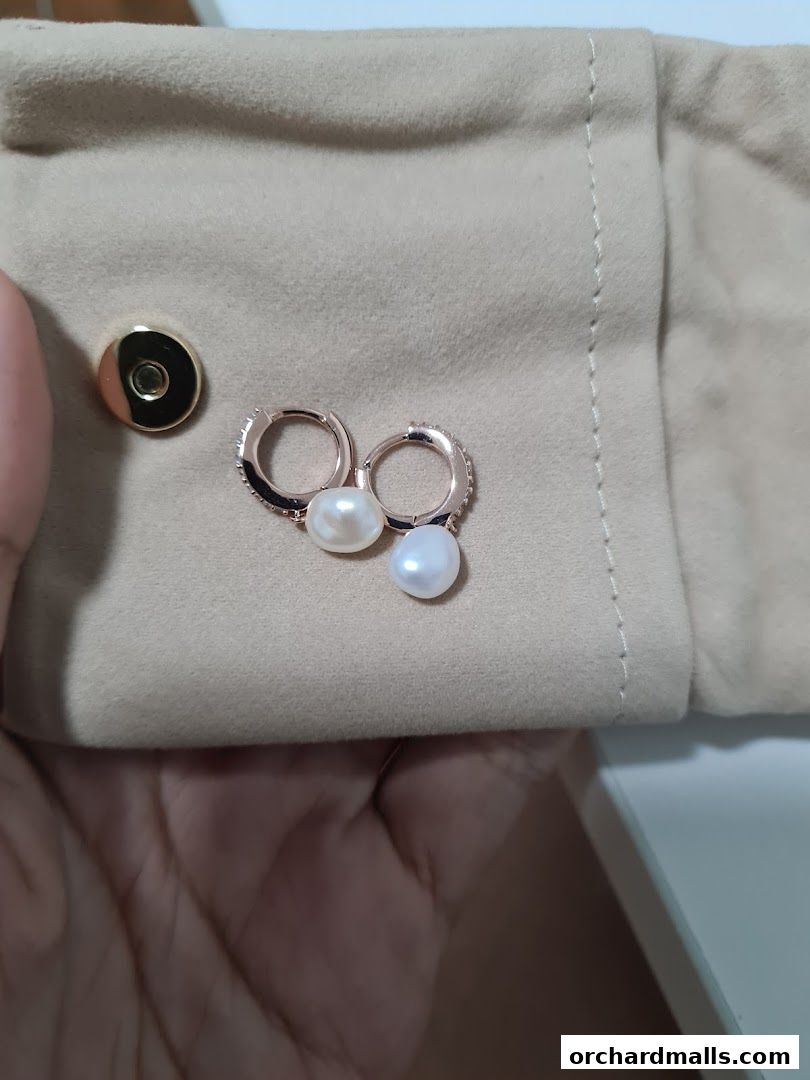 Close-up of pearl drop earrings with rose gold hoops on a beige fabric.