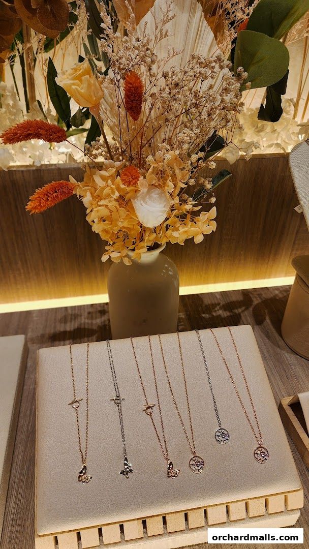 A display of delicate necklaces with butterfly and circular pendants, arranged on a stand with dried flowers.
