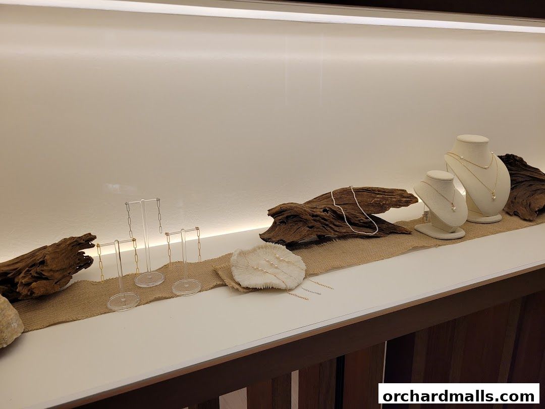 A display of pearl necklaces and jewelry stands on a shelf with driftwood accents.