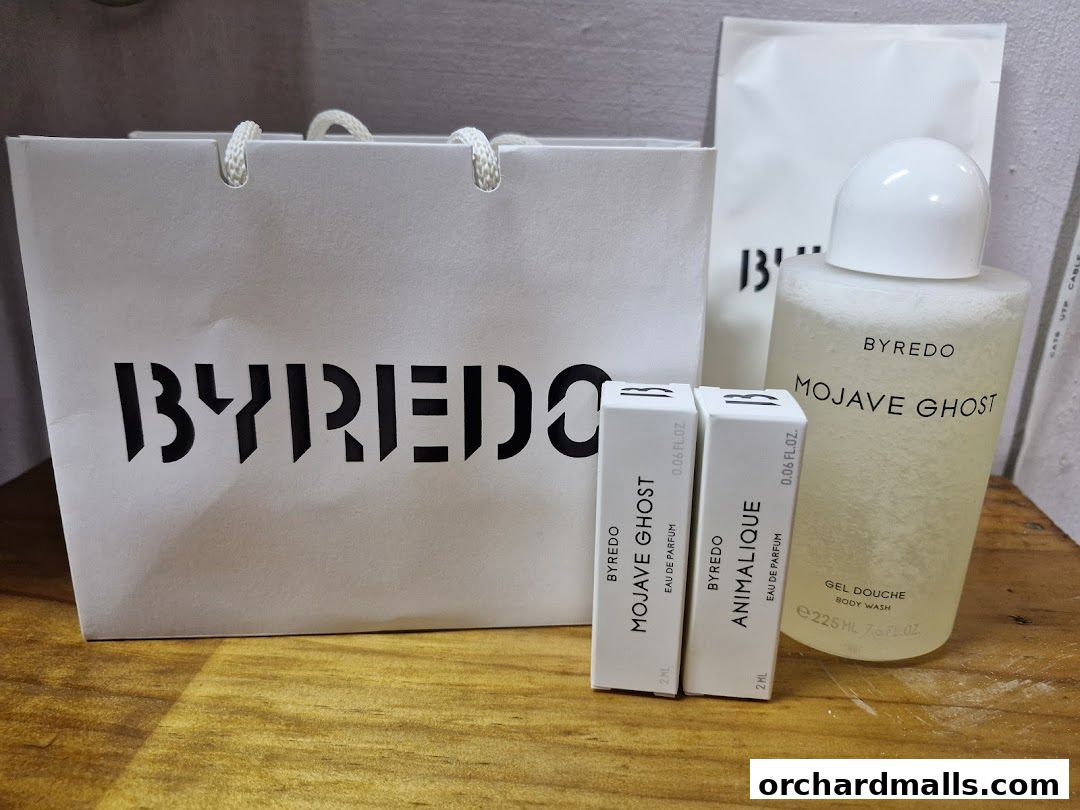Byredo shopping bag, perfume samples, and body wash on a wooden surface.