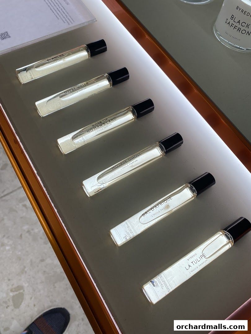 A display of Byredo perfume rollerballs in various scents on a lit shelf.