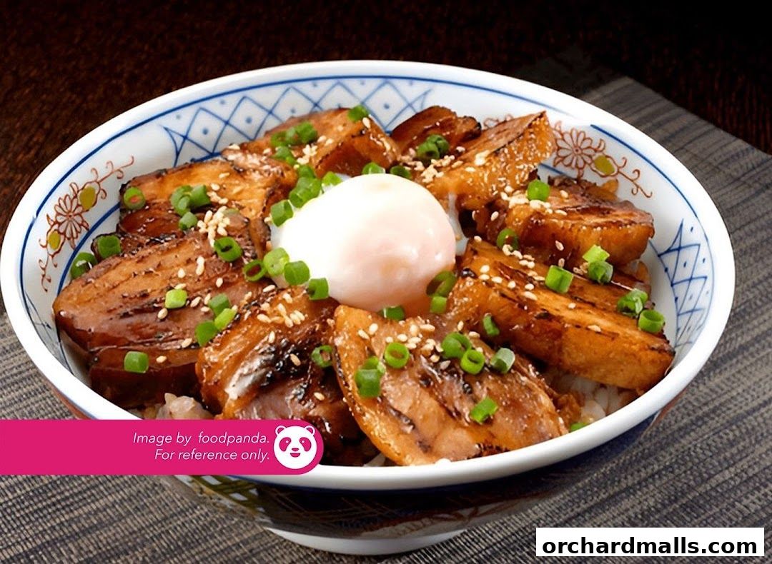 A bowl of rice topped with glazed pork belly and a soft-boiled egg, garnished with sesame seeds and scallions.