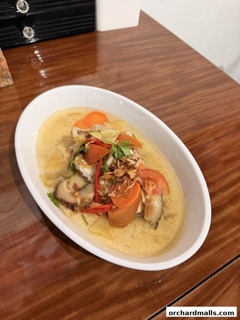 A bowl of flavorful soup with fish, vegetables, and herbs on a wooden table.