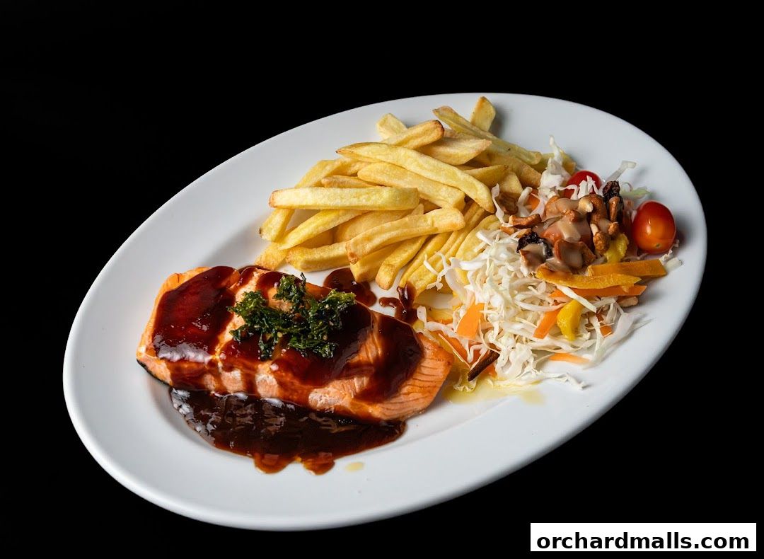A plate of salmon with fries and a side salad, drizzled with sauce.