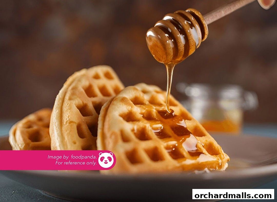 Golden waffles drizzled with honey on a plate, with a honey dipper.