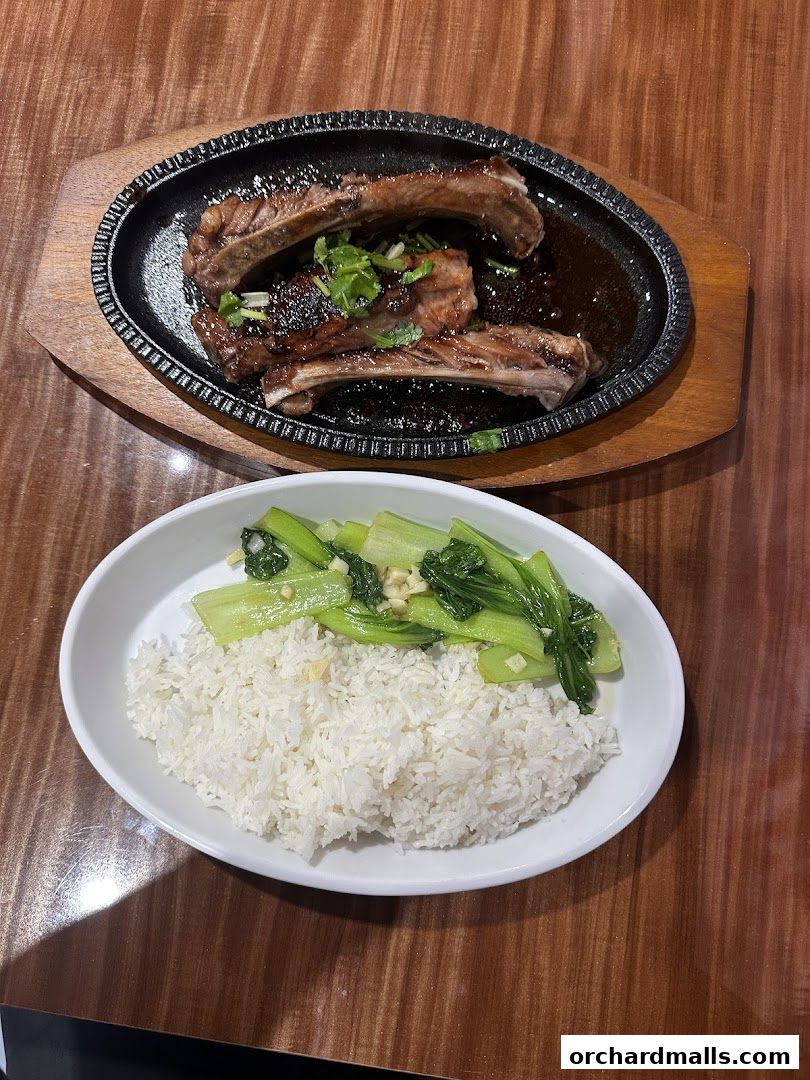 A sizzling plate of ribs served with steamed rice and stir-fried greens.