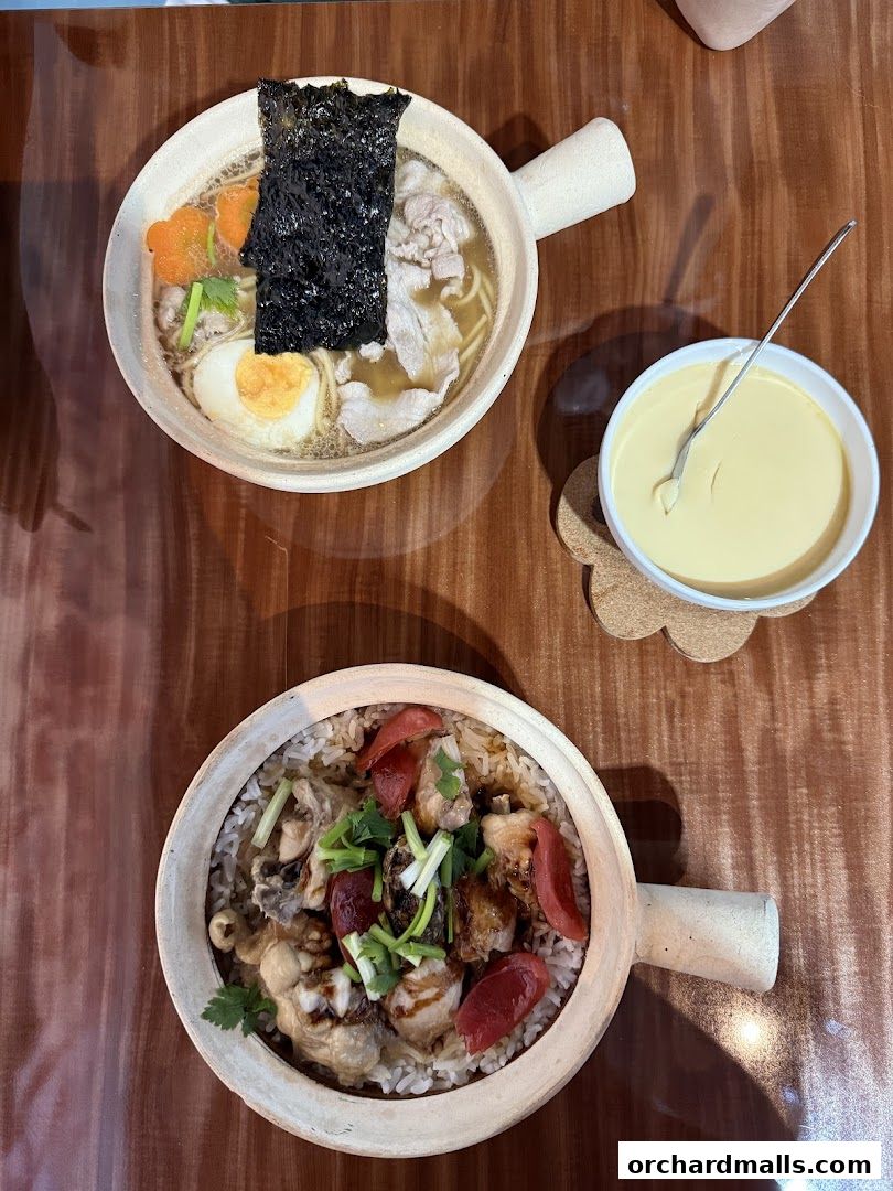 Two clay pot dishes and a bowl of steamed egg custard on a wooden table.