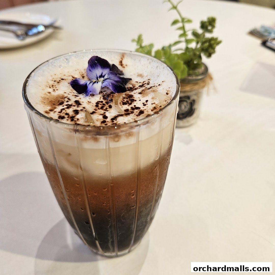 A layered iced coffee drink topped with foam, cocoa powder, and a purple flower.