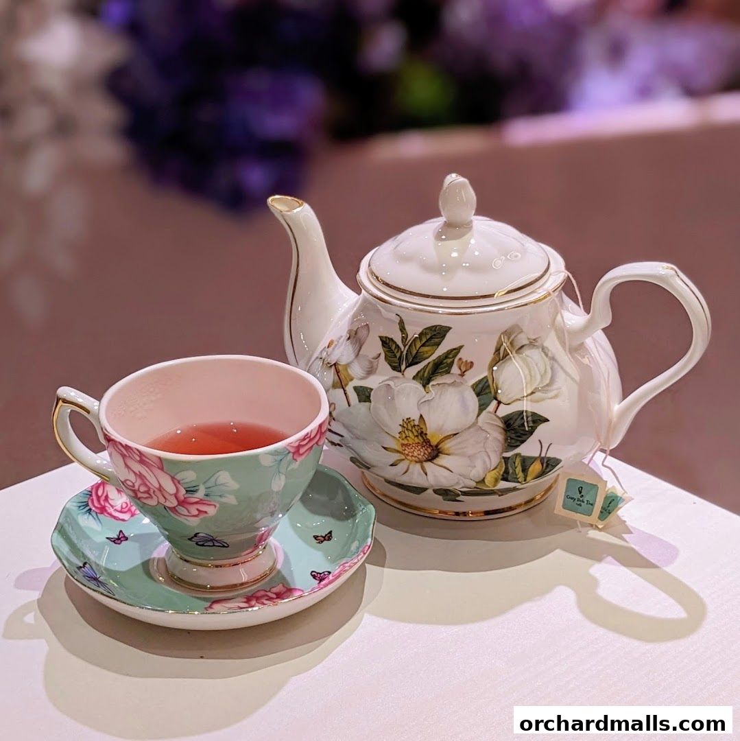 A beautifully decorated teapot and teacup filled with pink tea, set on a white table.