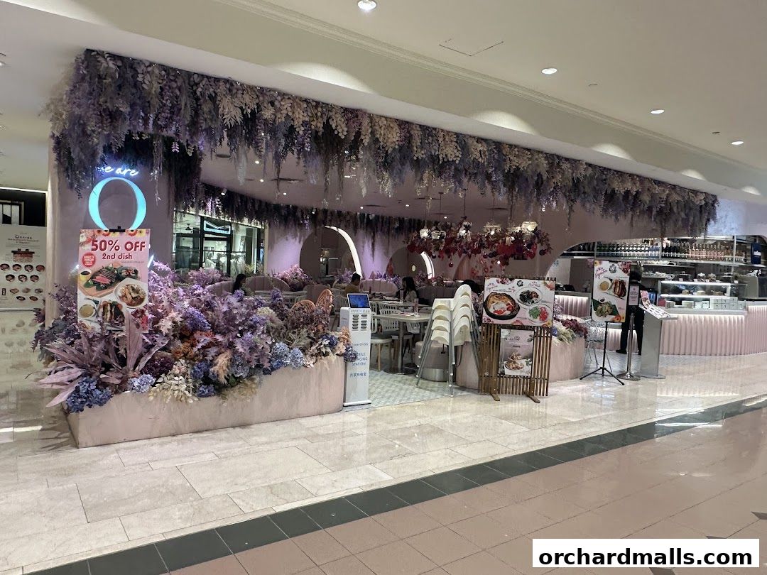 A beautifully decorated cafe entrance with floral arrangements and a 50% off promotion sign.