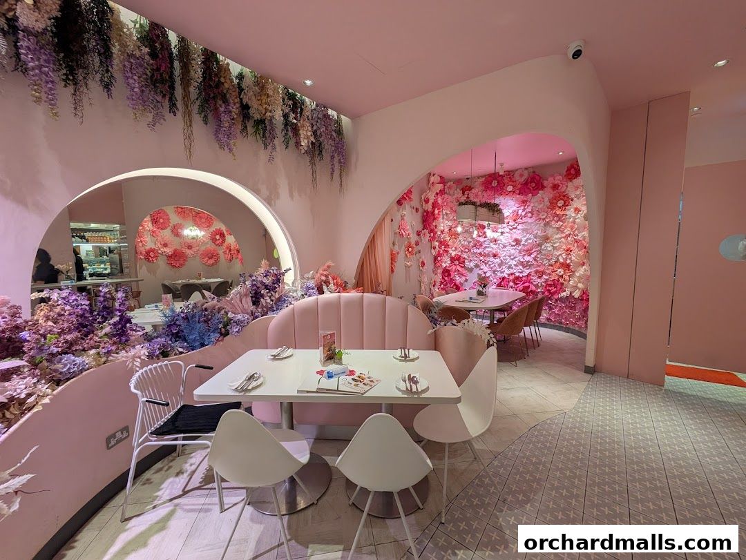 Interior of a stylish cafe with pink seating, floral decorations, and modern tables.