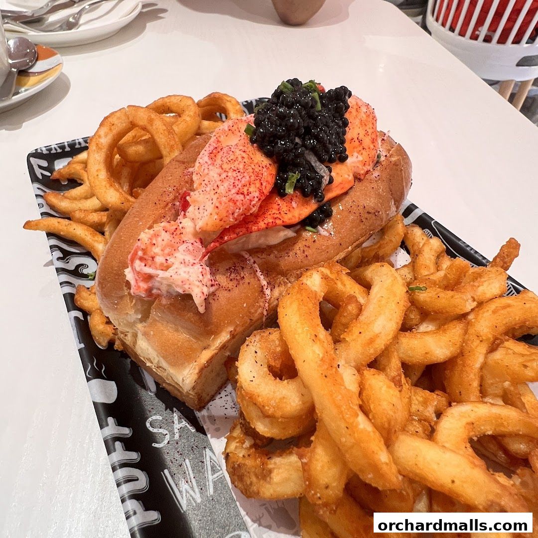 A gourmet lobster roll with caviar and curly fries served on a black and white patterned tray.