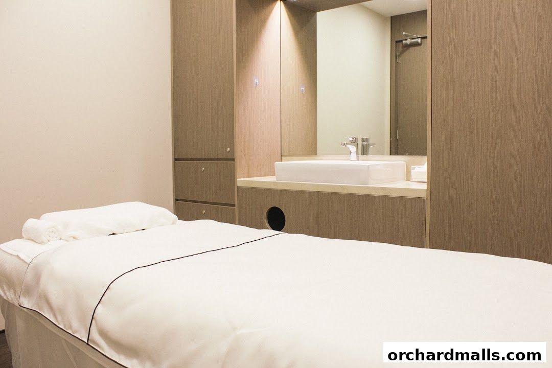 A clean and modern treatment room with a massage bed and a sink area.