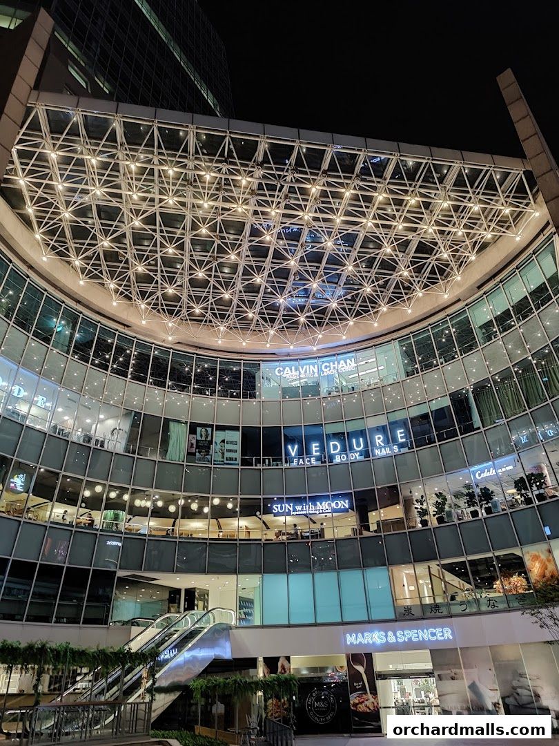 Exterior view of a modern shopping mall with multiple levels and illuminated storefronts at night.