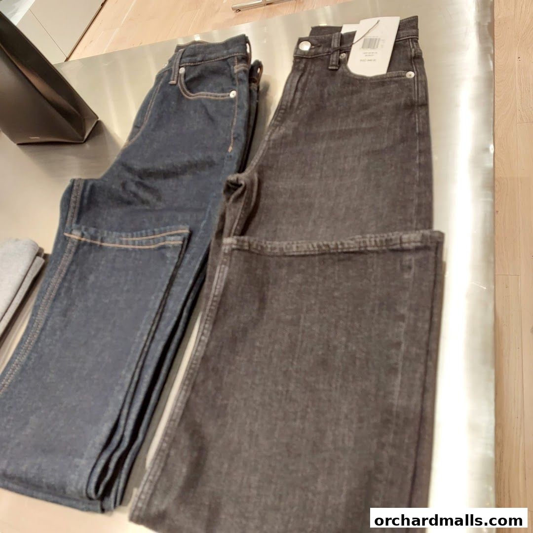 Two pairs of Calvin Klein jeans, one dark blue and one charcoal grey, displayed on a metallic surface.