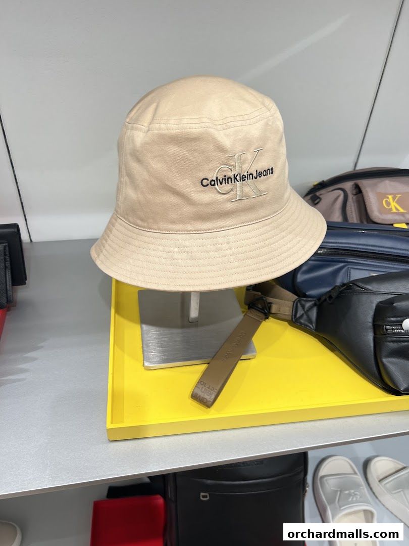 A Calvin Klein bucket hat with the brand's logo is displayed on a yellow stand.
