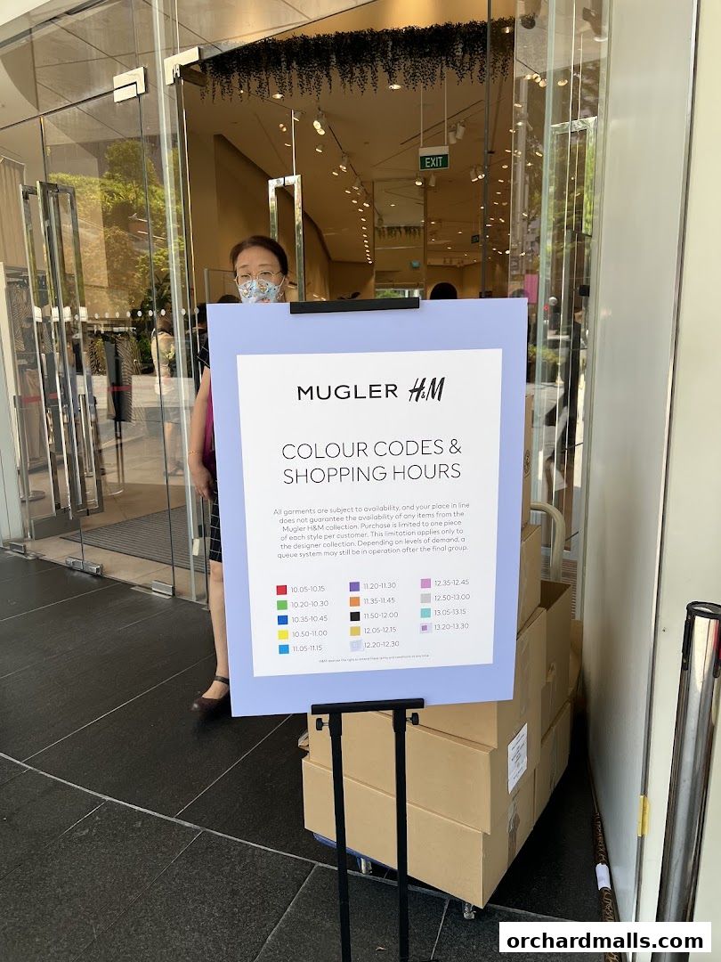 A sign displays Mugler H&M color codes and shopping hours outside a store entrance.