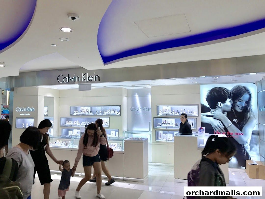 Calvin Klein store interior with watches and jewelry displays and customers.