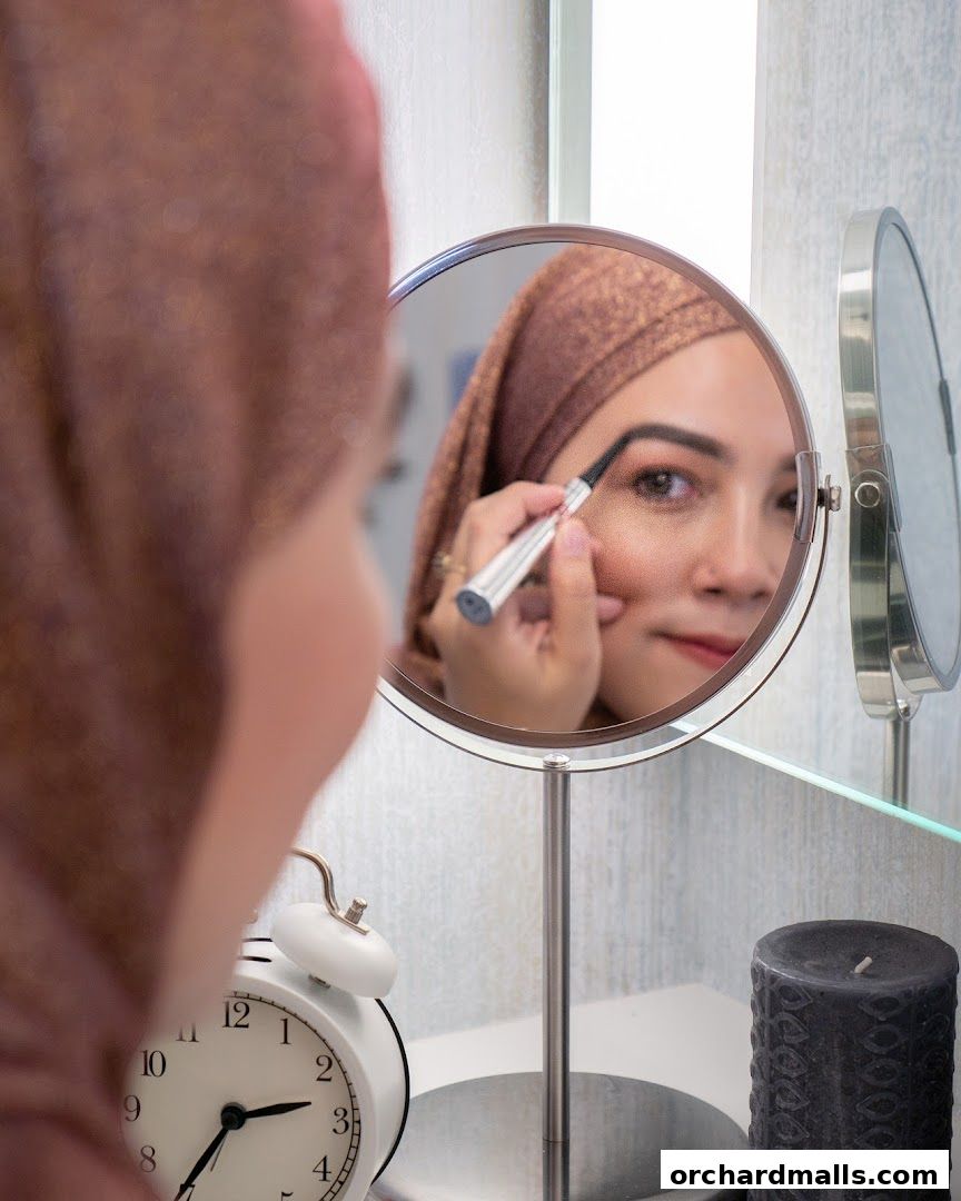 A woman in a hijab applies makeup in a mirror, with an alarm clock and candle nearby.