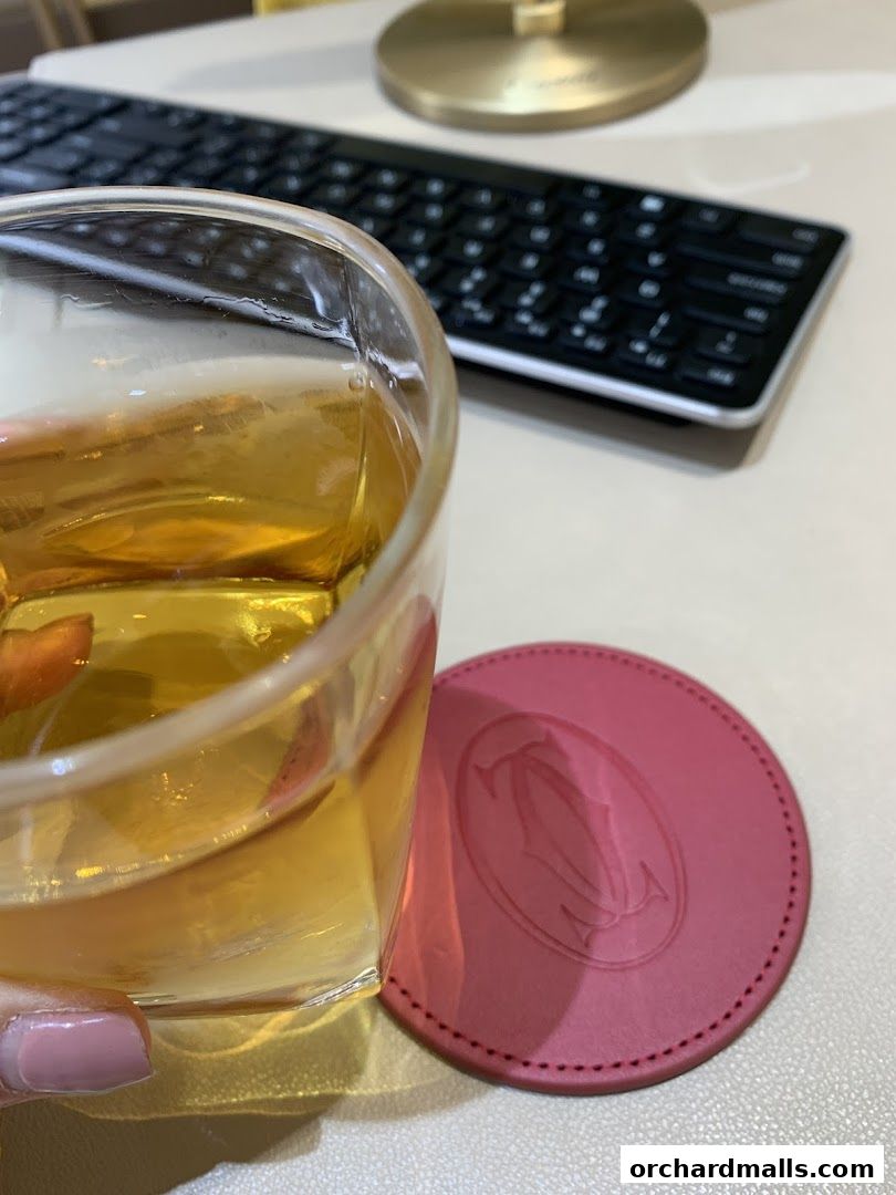 A glass of amber liquid sits on a pink Cartier coaster next to a keyboard.