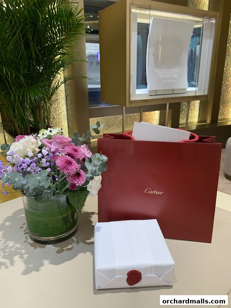 A Cartier shopping bag, a gift-wrapped item, and a floral arrangement on a table.