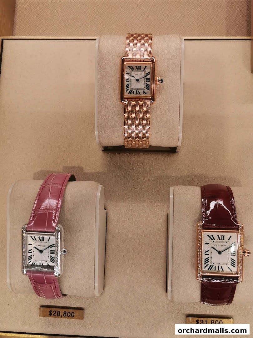 Three Cartier watches displayed on stands, two with price tags.