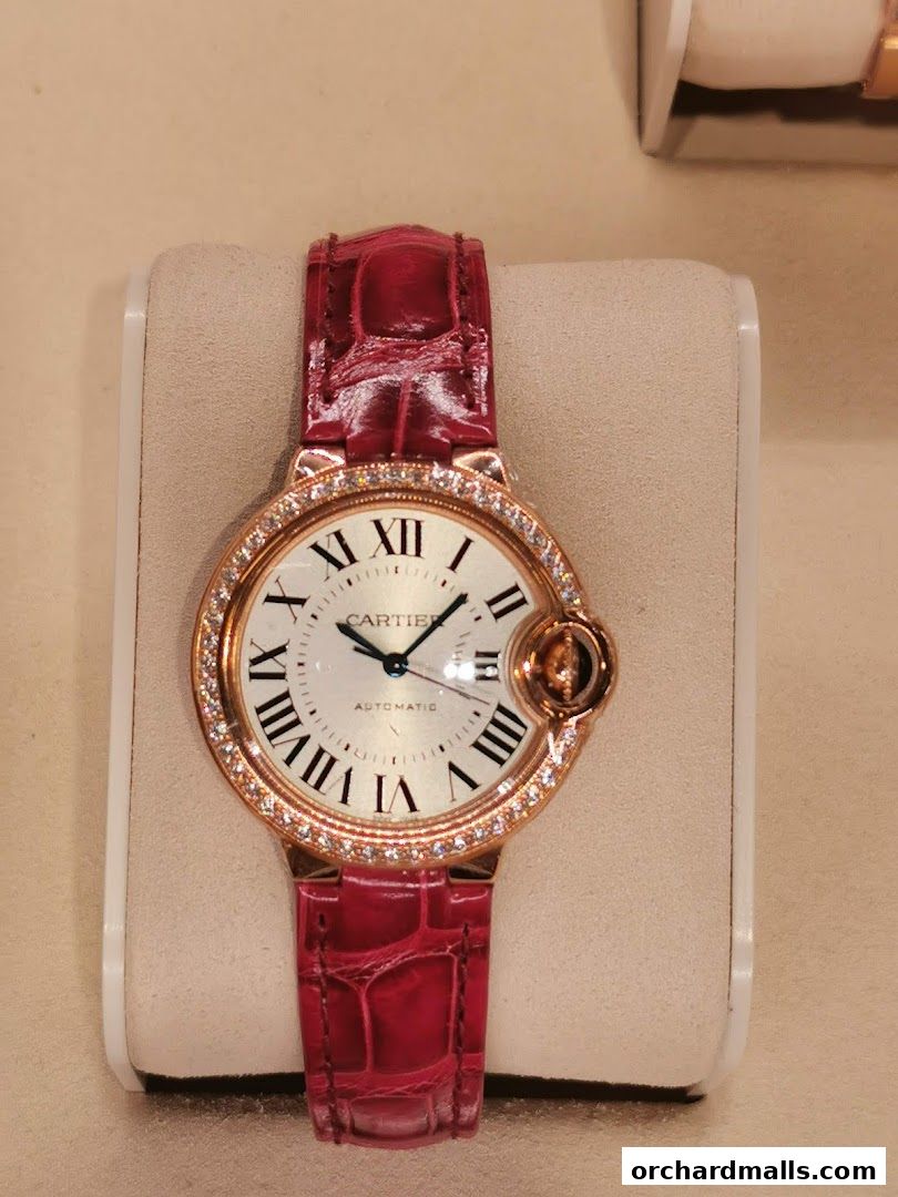 A close-up of a luxurious Cartier watch with a red alligator strap and diamond bezel.