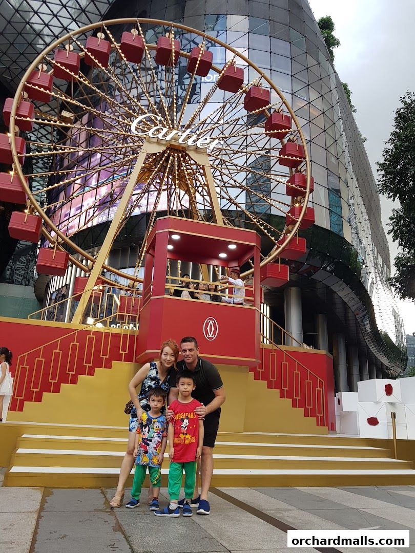 A family poses in front of a festive Cartier-themed Ferris wheel installation.