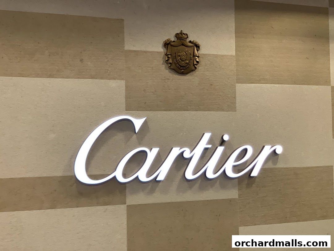 The illuminated Cartier logo is displayed on a textured wall with a crest above.