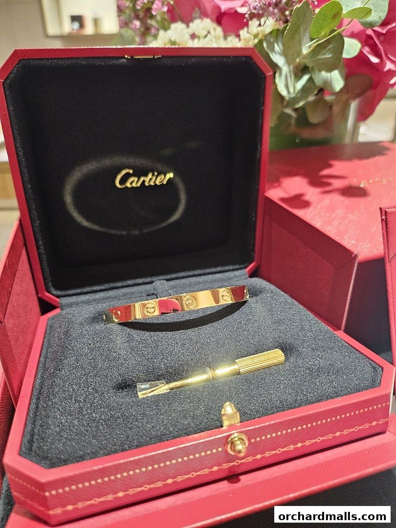A gold Cartier bracelet and screwdriver in a red Cartier jewelry box.