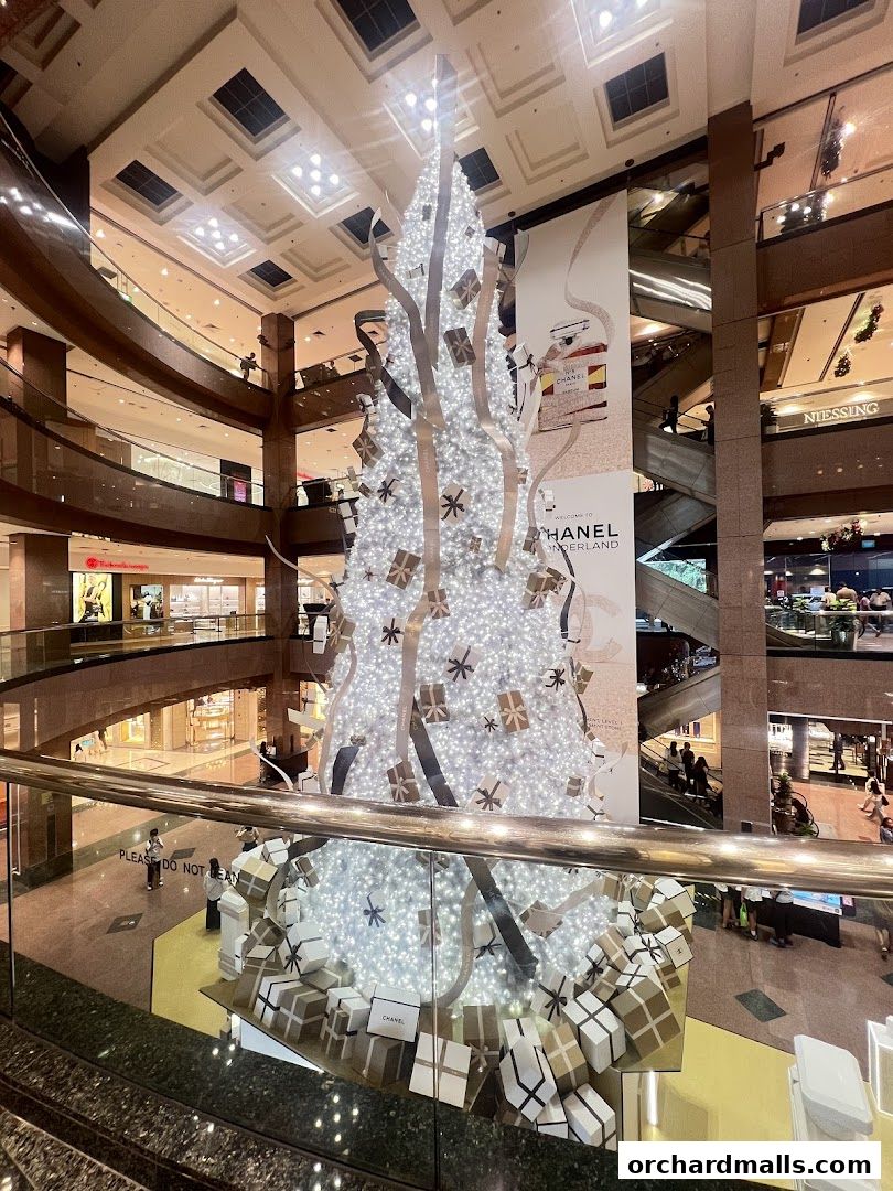 A large, illuminated Christmas tree decorated with gifts and ribbons in a shopping mall.