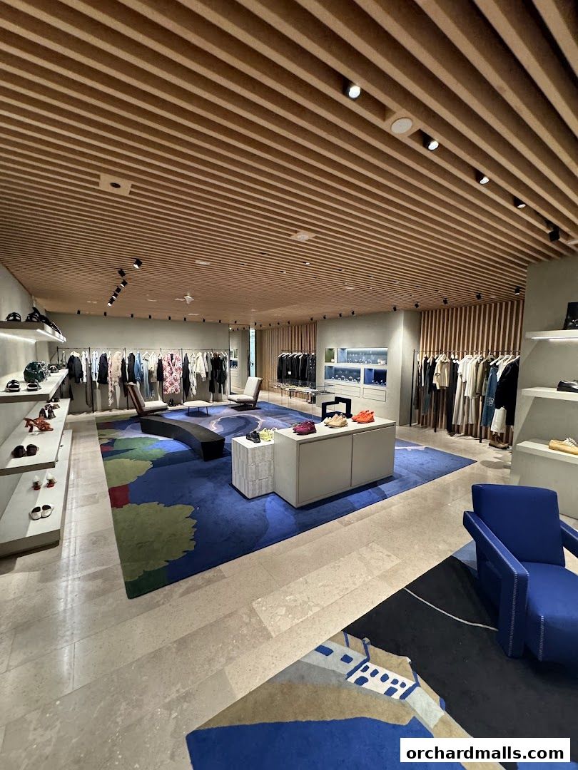 Interior view of a modern luxury fashion store with clothing racks, shoes, and seating.