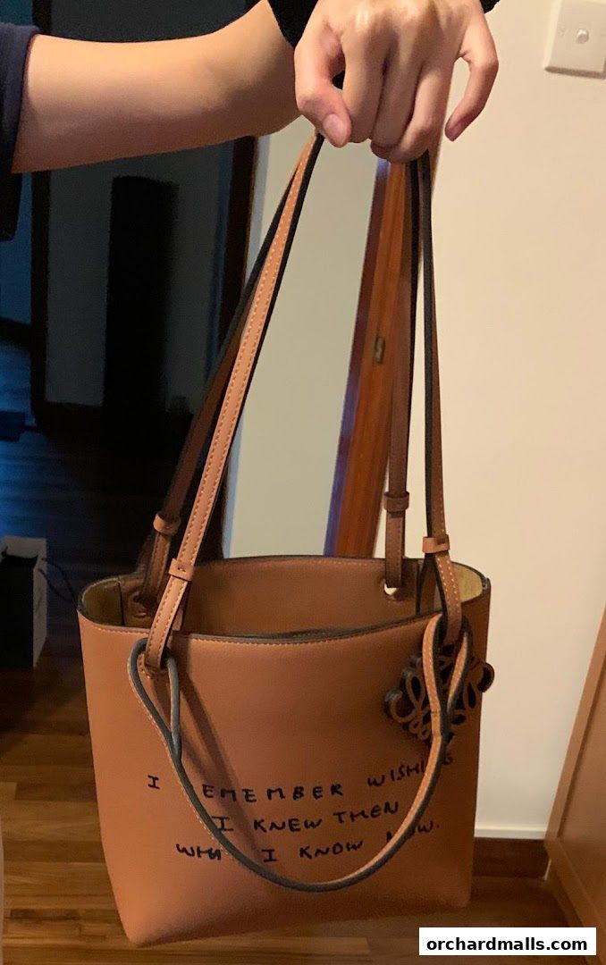 A person holds a tan leather tote bag with a quote written on it.