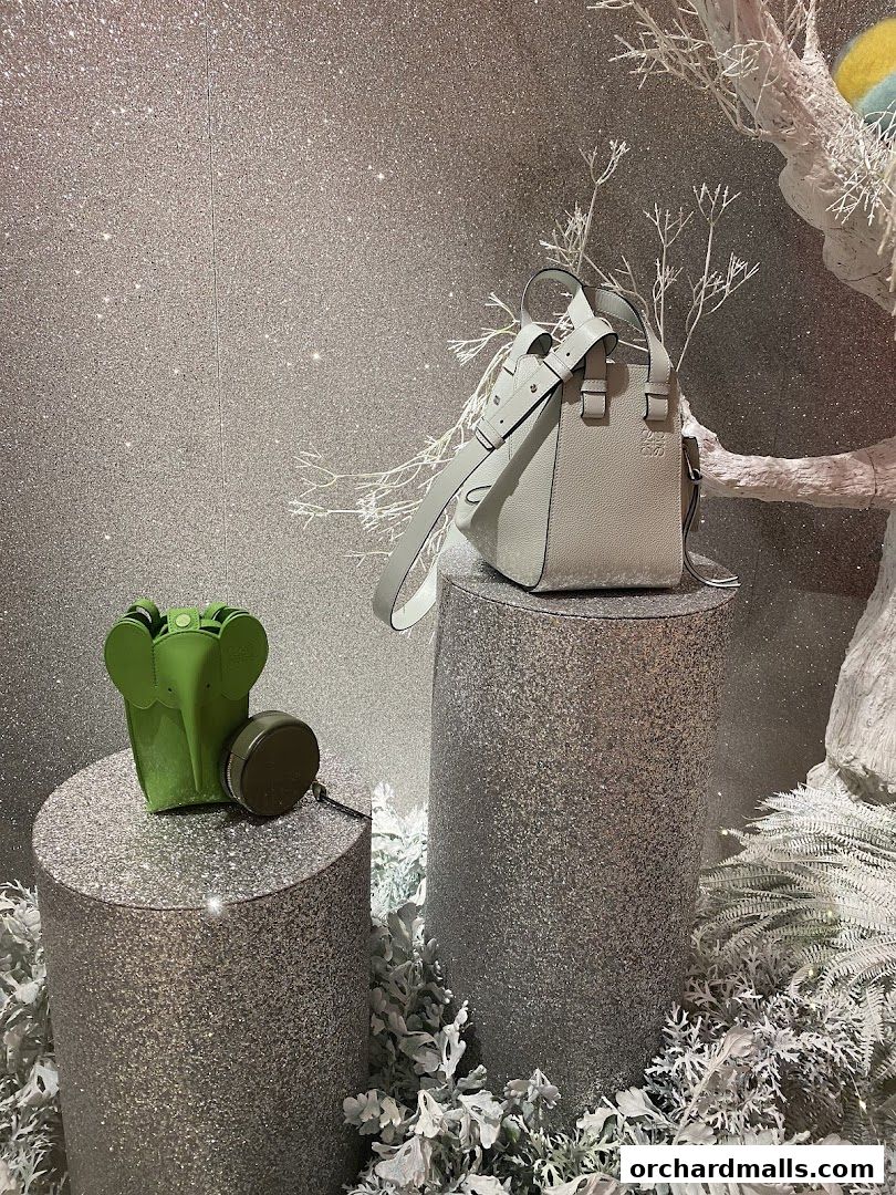 A display window featuring a grey Loewe handbag and a green elephant-shaped bag.
