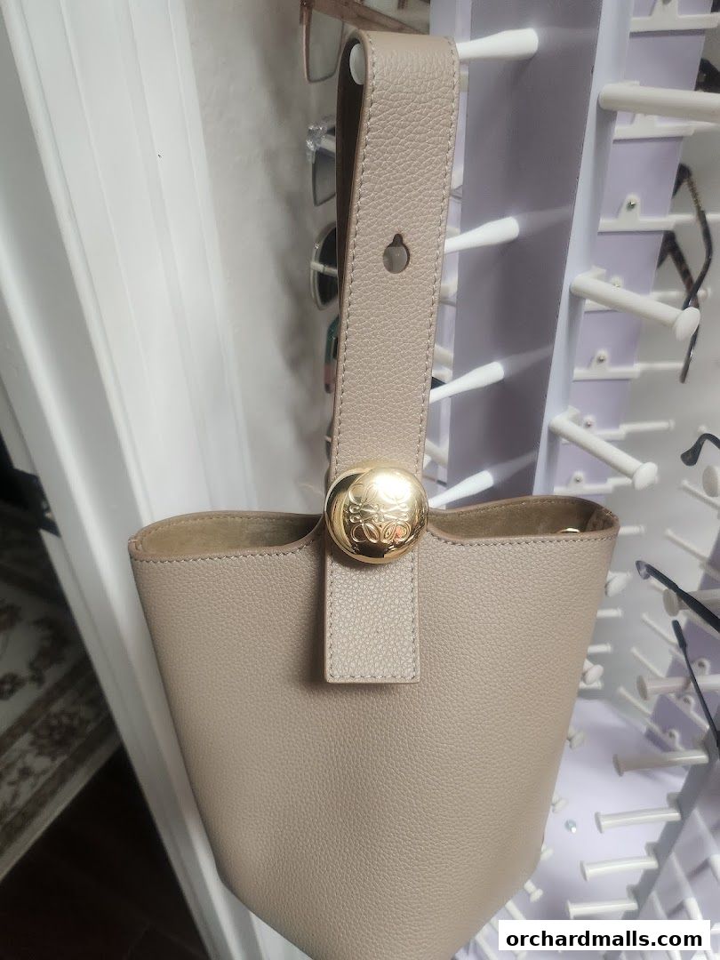 A close-up of a beige leather bucket bag with a gold logo closure.