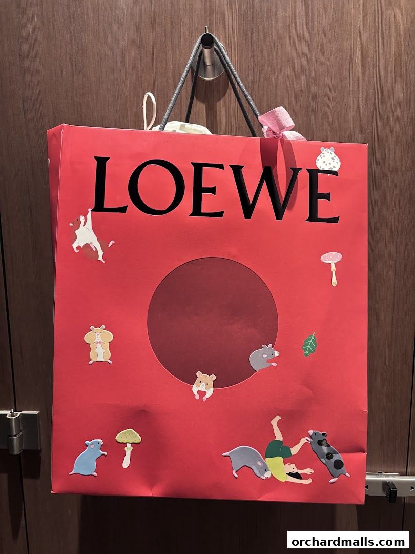 A red Loewe shopping bag with playful hamster and human illustrations.