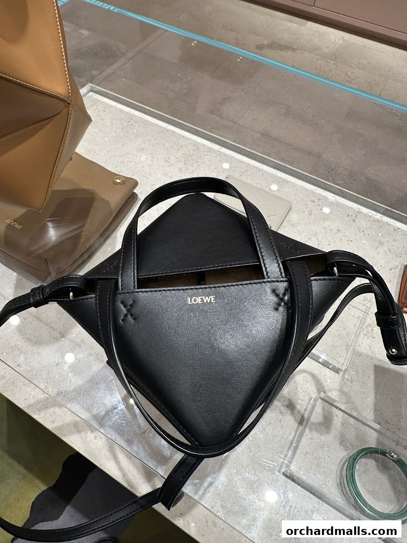 A black Loewe handbag with a unique geometric design is displayed on a glass surface.