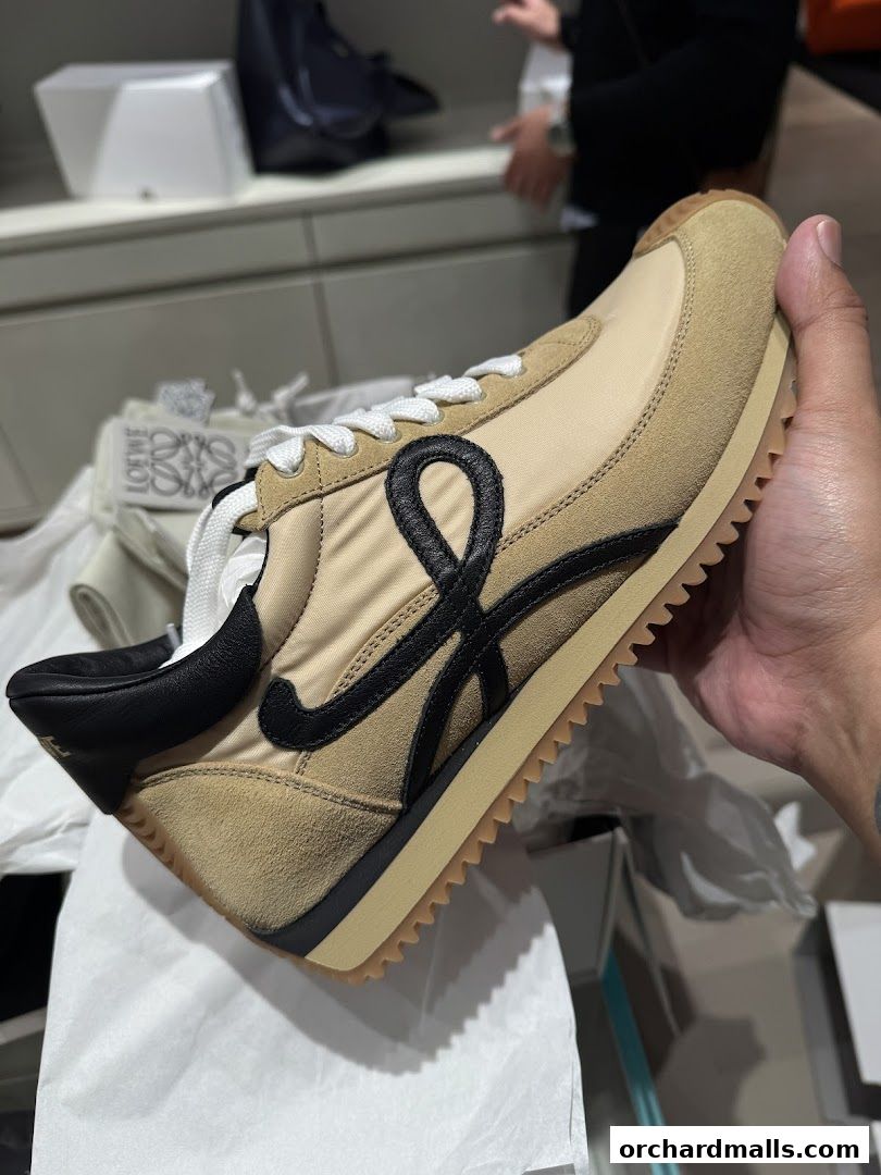 A hand holds a beige and black Loewe sneaker with the signature 'L' logo.