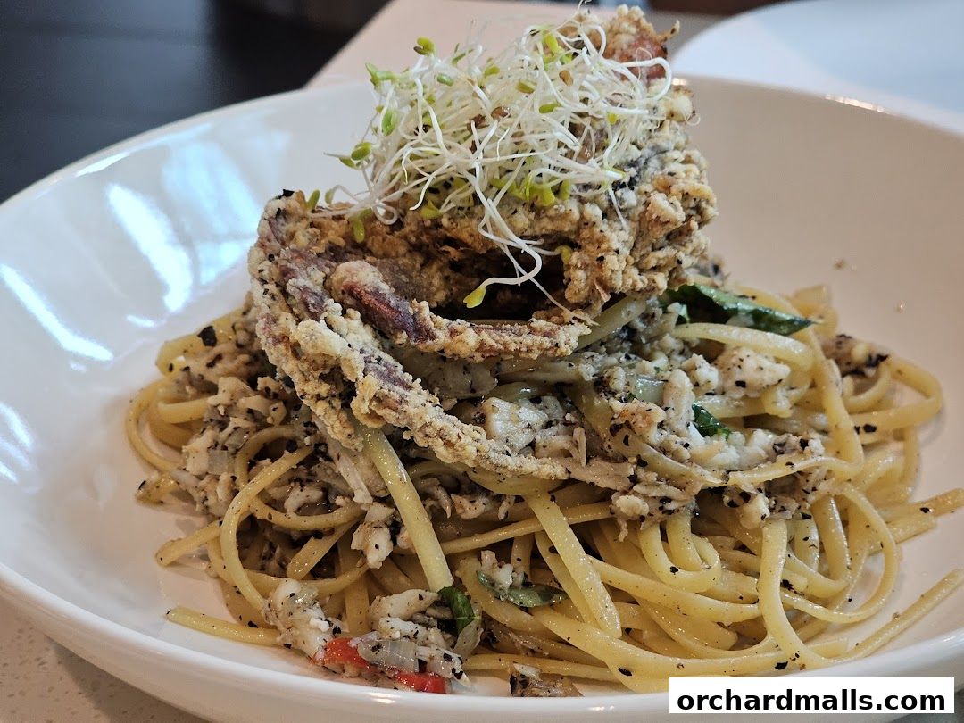 A close-up of a pasta dish topped with a crispy soft-shell crab and sprouts.