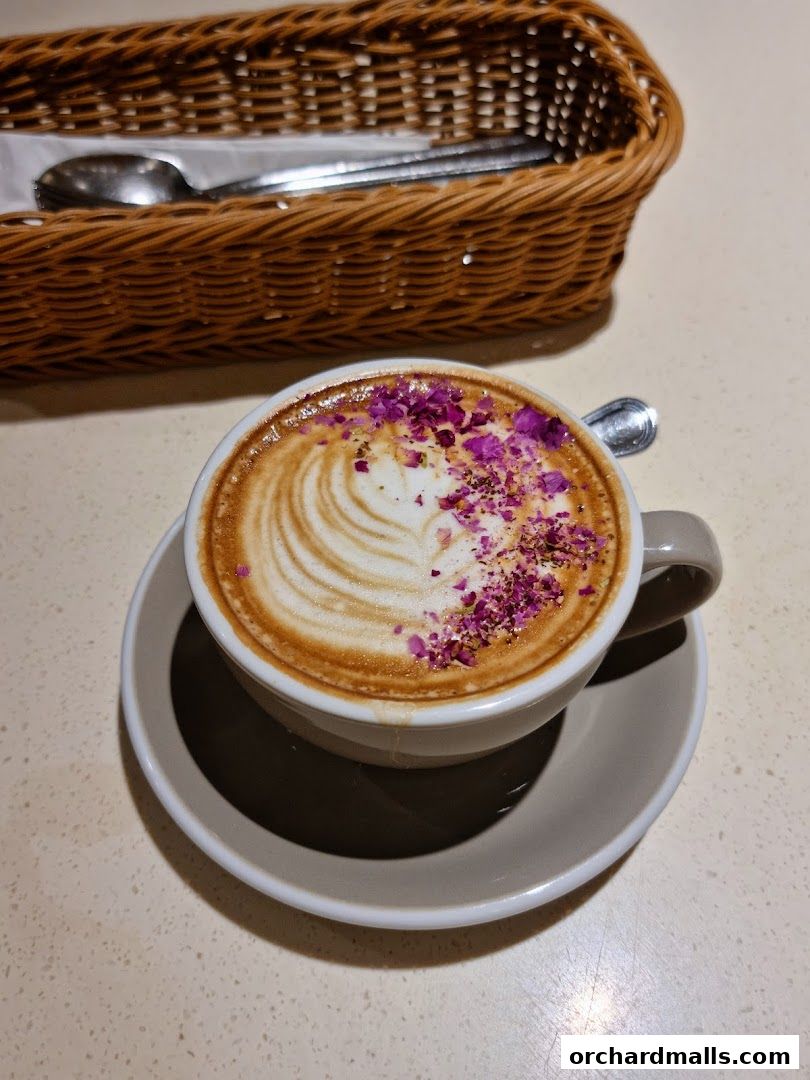 A beautifully crafted latte with rose petals and latte art, served with a basket of cutlery.