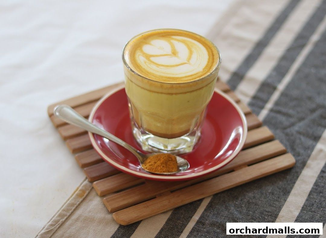 A golden turmeric latte with latte art, served with a spoon of turmeric powder.