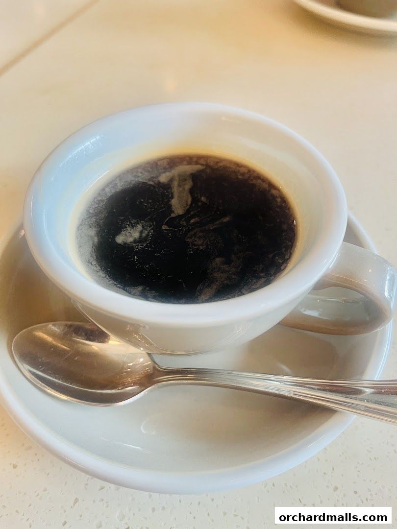 A close-up shot of a steaming cup of black coffee with a spoon on a saucer.