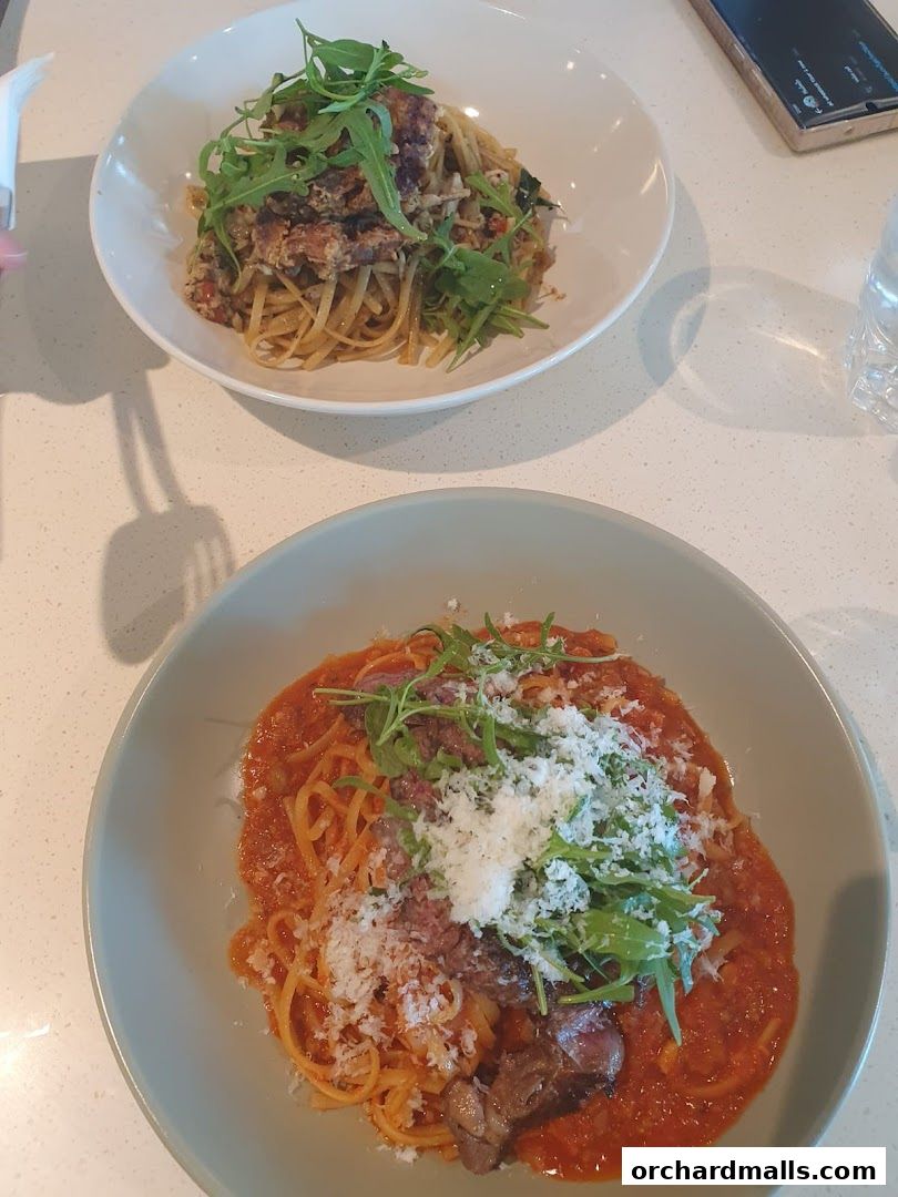 Two bowls of pasta dishes, one with a rich tomato sauce and meat, the other with a lighter sauce and greens.